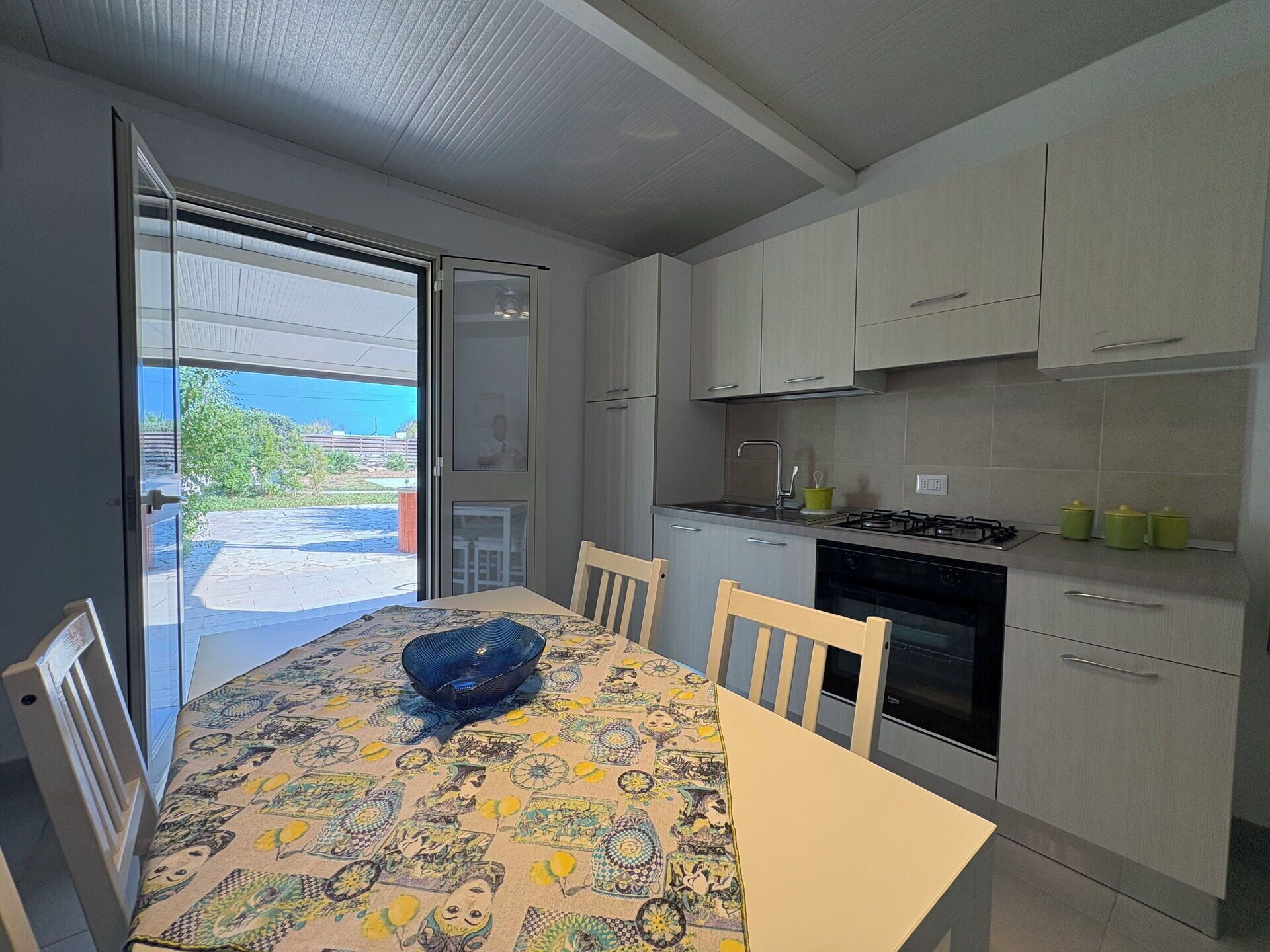 A modern kitchen with a dining table, chairs, and a view through a glass door.