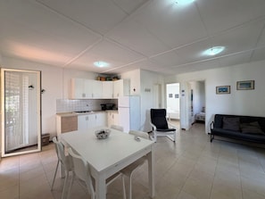 A modern kitchen with white cabinets, a dining table with chairs, a black office chair, and a sofa in a living area. - Villa in Marina Di Ragusa with 3 bedrooms sleeps 7 (Marina Di Ragusa)