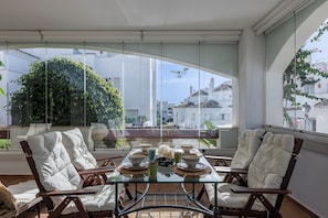 A dining area with a glass table, white cushioned chairs, and a view of buildings and greenery through large windows. - Aloha Royal Marbella, 2BR Wonderful apartment in Nueva Andalucia (Marbella)