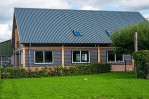A modern two-story house with a sloped metal roof, large windows, and a well-maintained lawn.