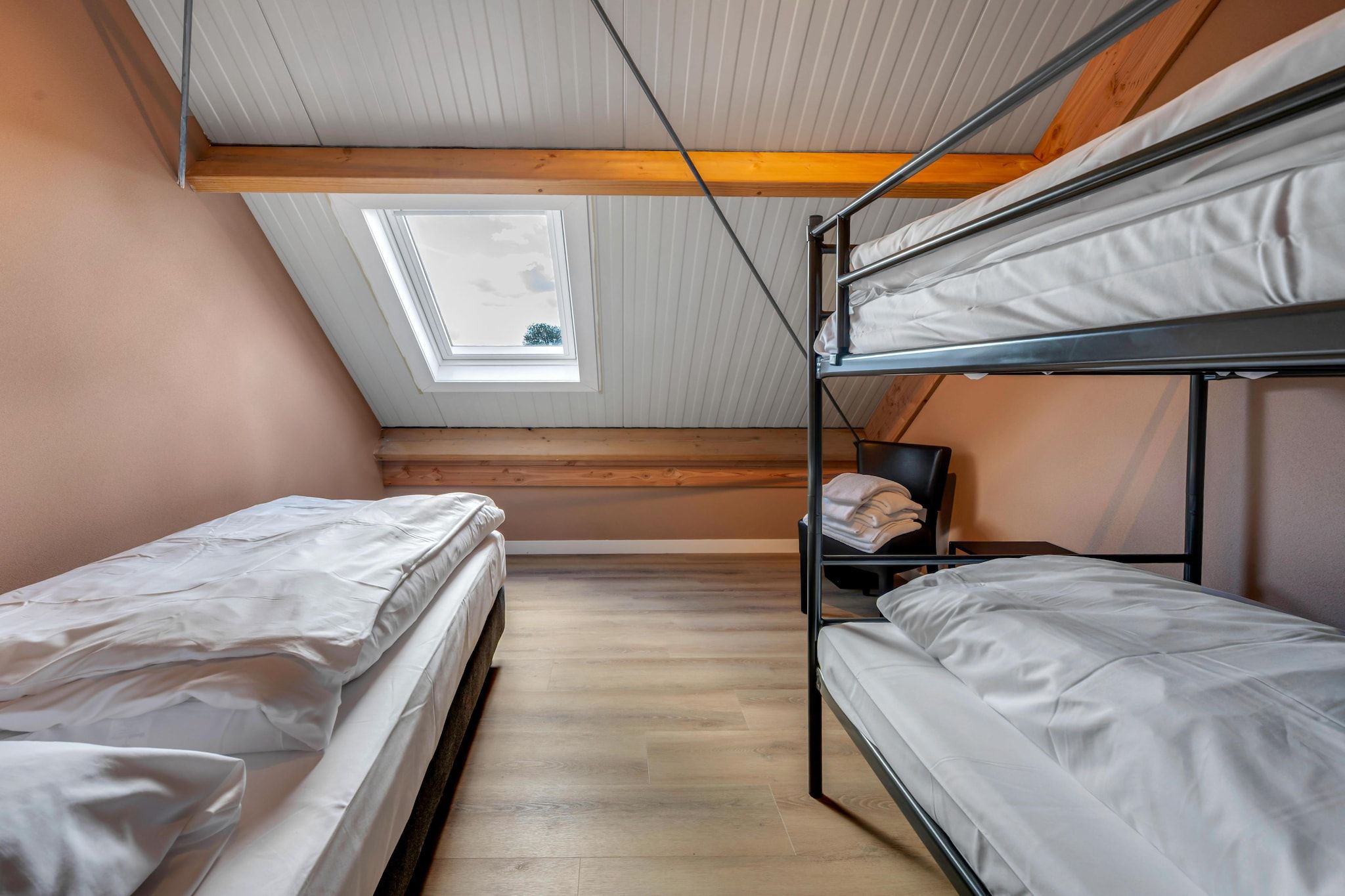 Une chambre de dortoir avec des lits superposés, une lucarne et un plancher en bois.