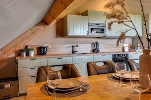 A kitchen with a dining area, featuring a wooden table set for two, a stove, and a microwave.