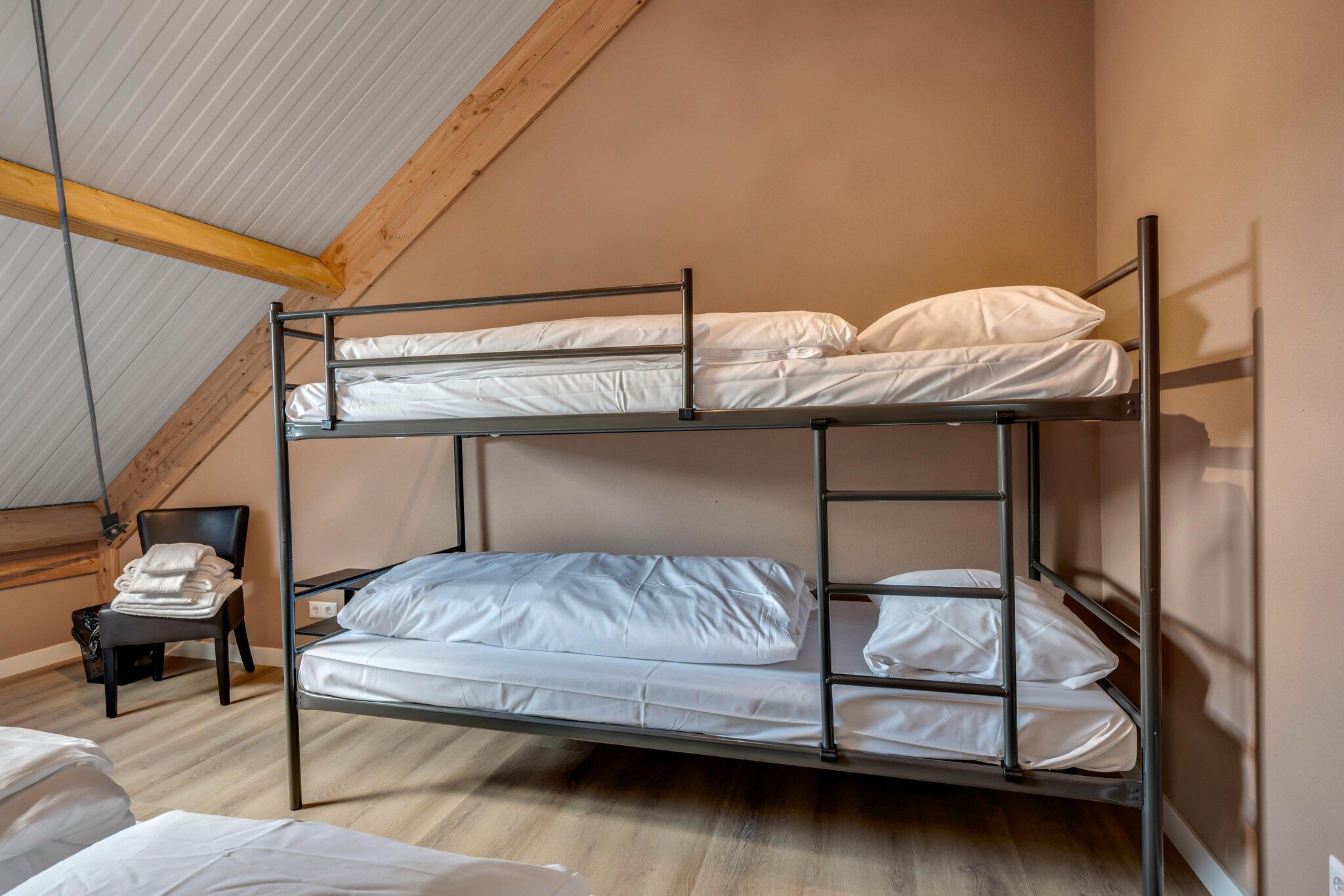Una cama individual en un dormitorio con techo inclinado y una silla con toallas.