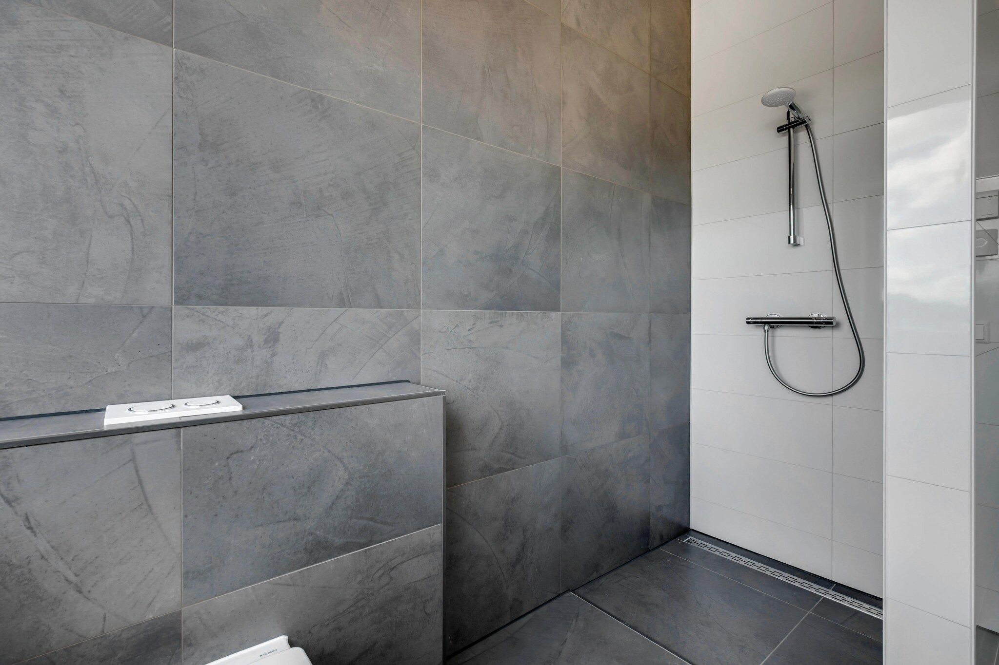 A modern bathroom with grey tiles, a shower, and a white countertop with a sign.