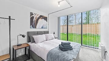 A modern bedroom with a large bed, a bedside table, a floor lamp, and a view of the outdoors.