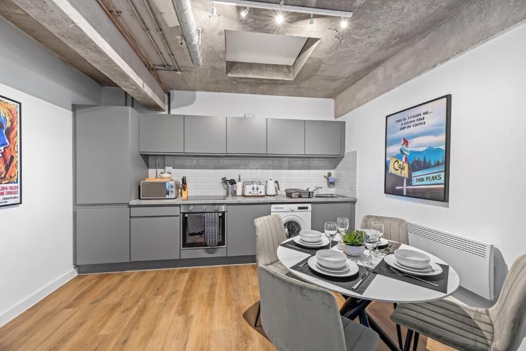 A modern kitchen with grey cabinets, a dining area with a table set for two, and a poster on the wall.
