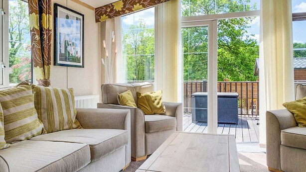 A modern living room with a sofa, armchairs, and a coffee table. There is a large window with a view of greenery outside.