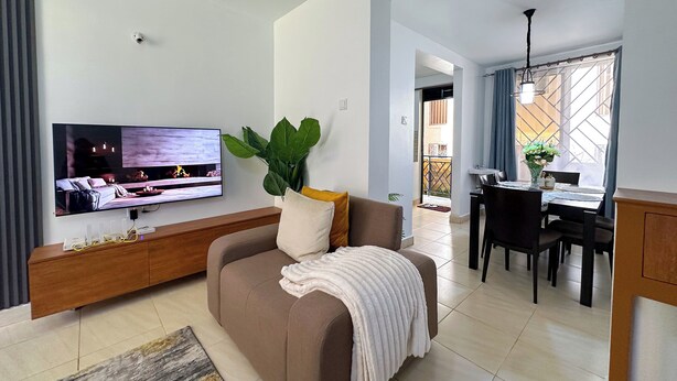 A living room with a sofa, TV, wooden cabinet, and a dining area with a table and chairs. - The snug cove, beautifully furnished and fully functional. Family friendly! (Najjera)