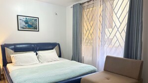 A bedroom with a bed, a chair, a window with curtains, and a framed picture on the wall. - The snug cove, beautifully furnished and fully functional. Family friendly! (Najjera)