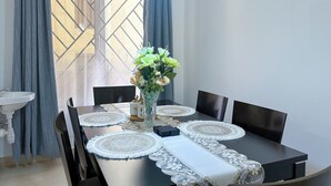 A dining table with placemats, chairs, a vase with flowers, and a window with curtains. - The snug cove, beautifully furnished and fully functional. Family friendly! (Najjera)