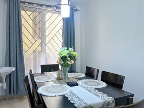 Ein Esstisch mit Platzsets, Stühlen, einer Blumenvase und einem Fenster mit Vorhängen.