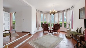 Una habitación con techo abovedado, una araña, dos sillones, una mesita, un sofá y una alfombra grande.