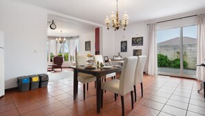 Un comedor con una mesa, sillas, una araña y vistas a través de un vidrio.