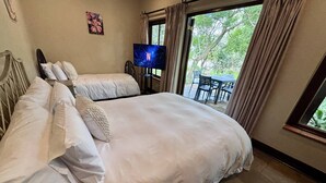 A double bed with white bedding, a television on a stand, and a view of an outdoor patio with a table and chairs. - Staynest Guesthouse GP (Johannesburg)