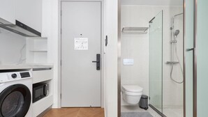 Een kleine badkamer met een douche, toilet en een wasmachine.