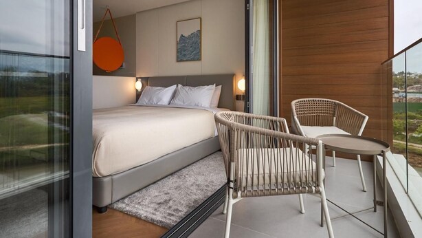 Een moderne slaapkamer met een bed, twee stoelen, een tafeltje en uitzicht op de omgeving.
