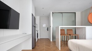 Een moderne hotelkamer met een flatscreen-tv, een bed, een zithoek met twee stoelen en een wasmachine op de achtergrond.