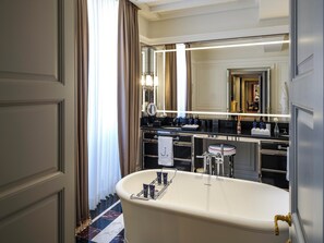 A luxurious bathroom with a freestanding bathtub, a large mirror, and a vanity with a sink and towel rack. - Casa J.K. Place Roma (Rome)