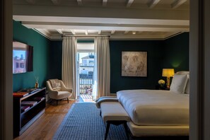 A hotel room with a bed, a chair, a desk with books, a painting on the wall, and a view through the curtains. - Casa J.K. Place Roma (Rome)