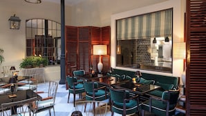 A spacious indoor area with a high ceiling, a large window with green curtains, and a seating area with green upholstered chairs and a table.
