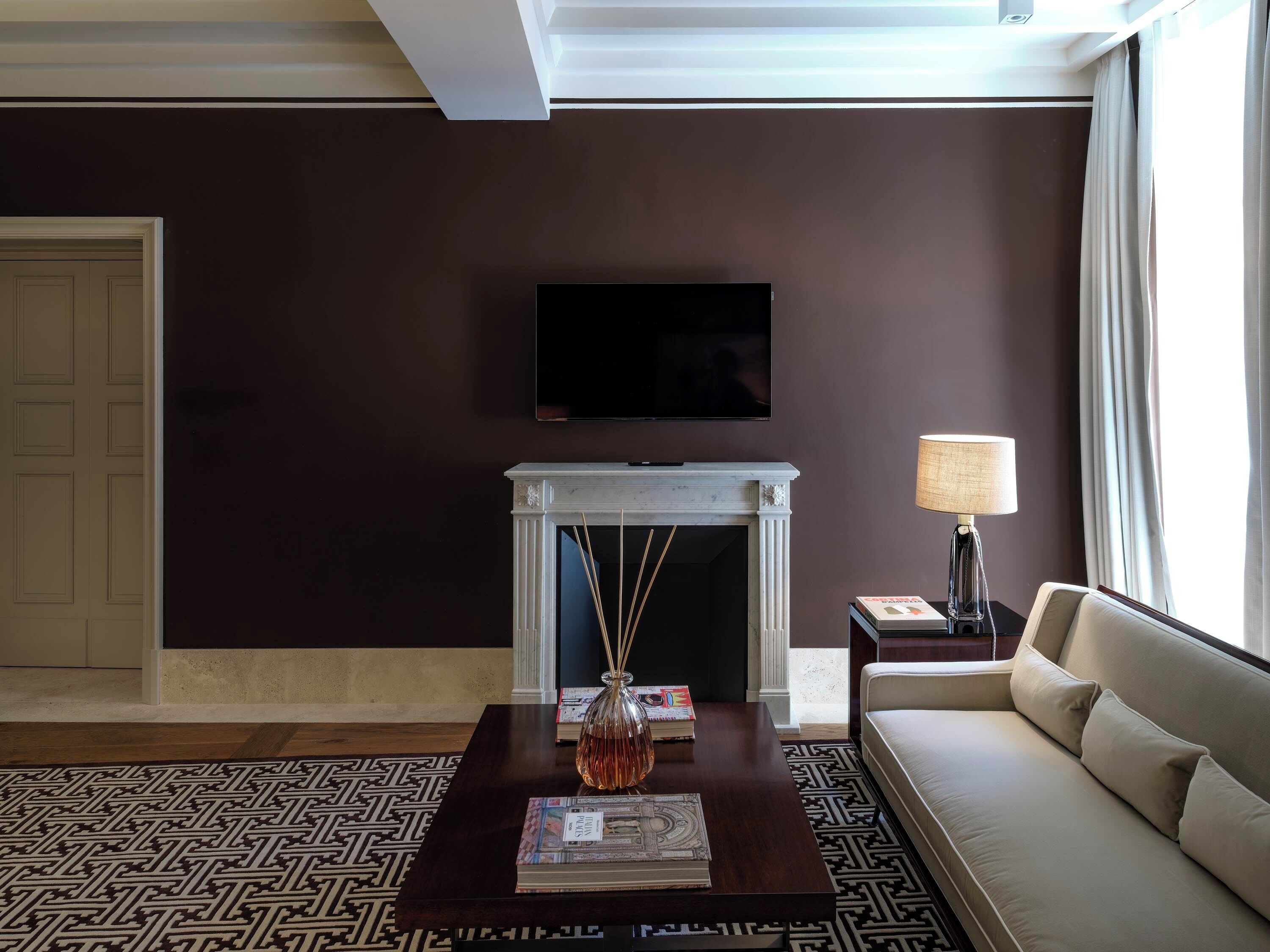 A living room with a fireplace, a sofa, a coffee table with magazines, a lamp, and a television on the wall.