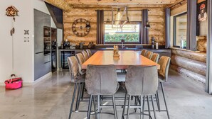 A modern kitchen with a wooden interior, a large dining table with chairs, and a clock on the wall.