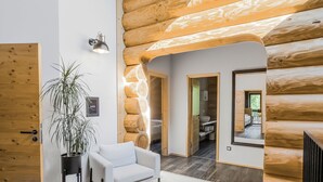 A modern log cabin interior with a white sofa, a potted plant, and a large mirror reflecting the room.