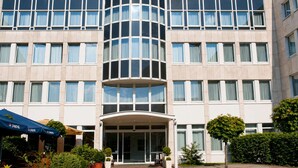 Um hotel com vários andares, fachada de vidro curva, entrada coberta e área externa para sentar com a marca Pepsi.