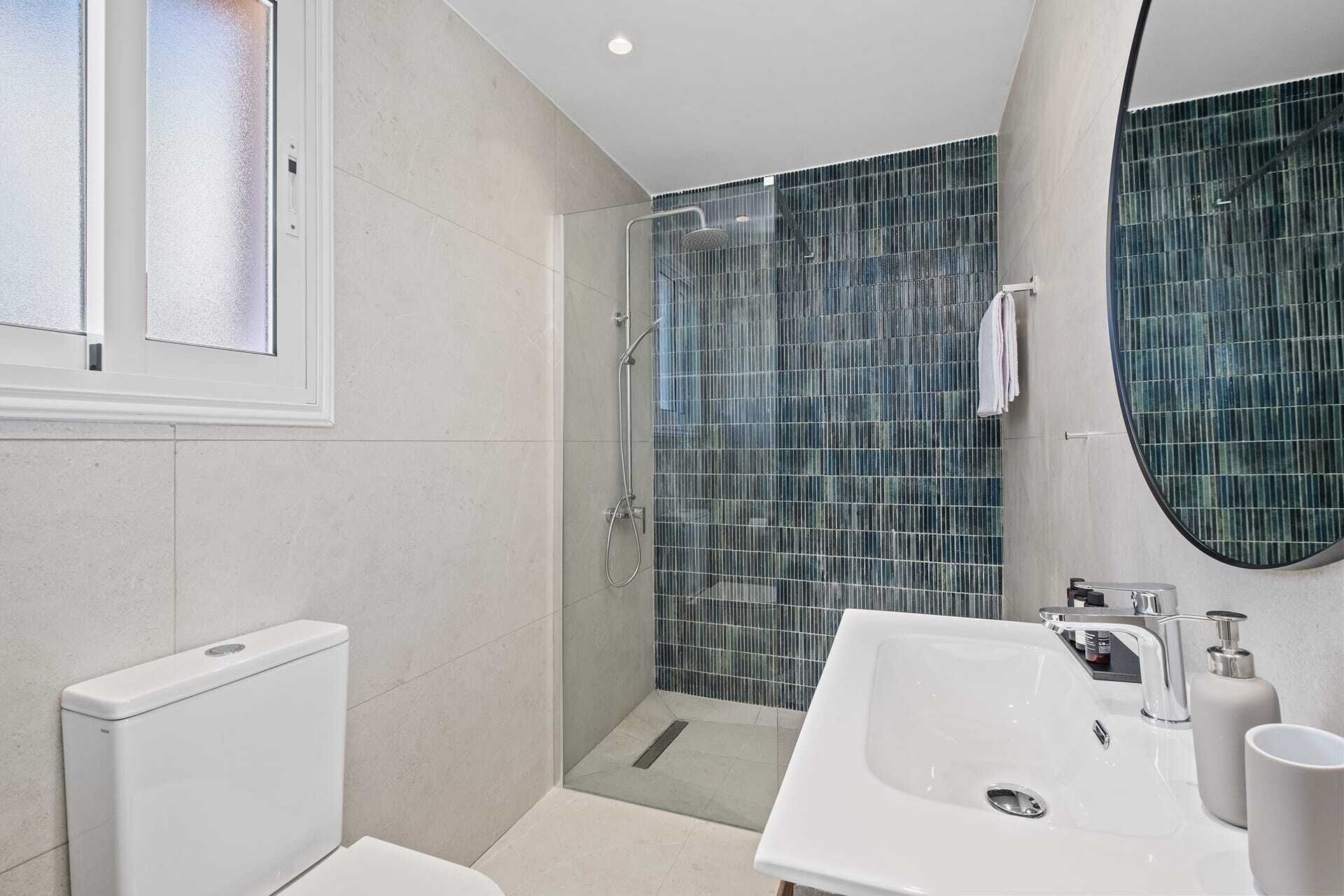 Un baño moderno con cabina de ducha de vidrio, un lavamanos blanco y un inodoro.