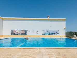 En swimmingpool med en väggmålning, en klarblå himmel och ett däck med kakelplattor.