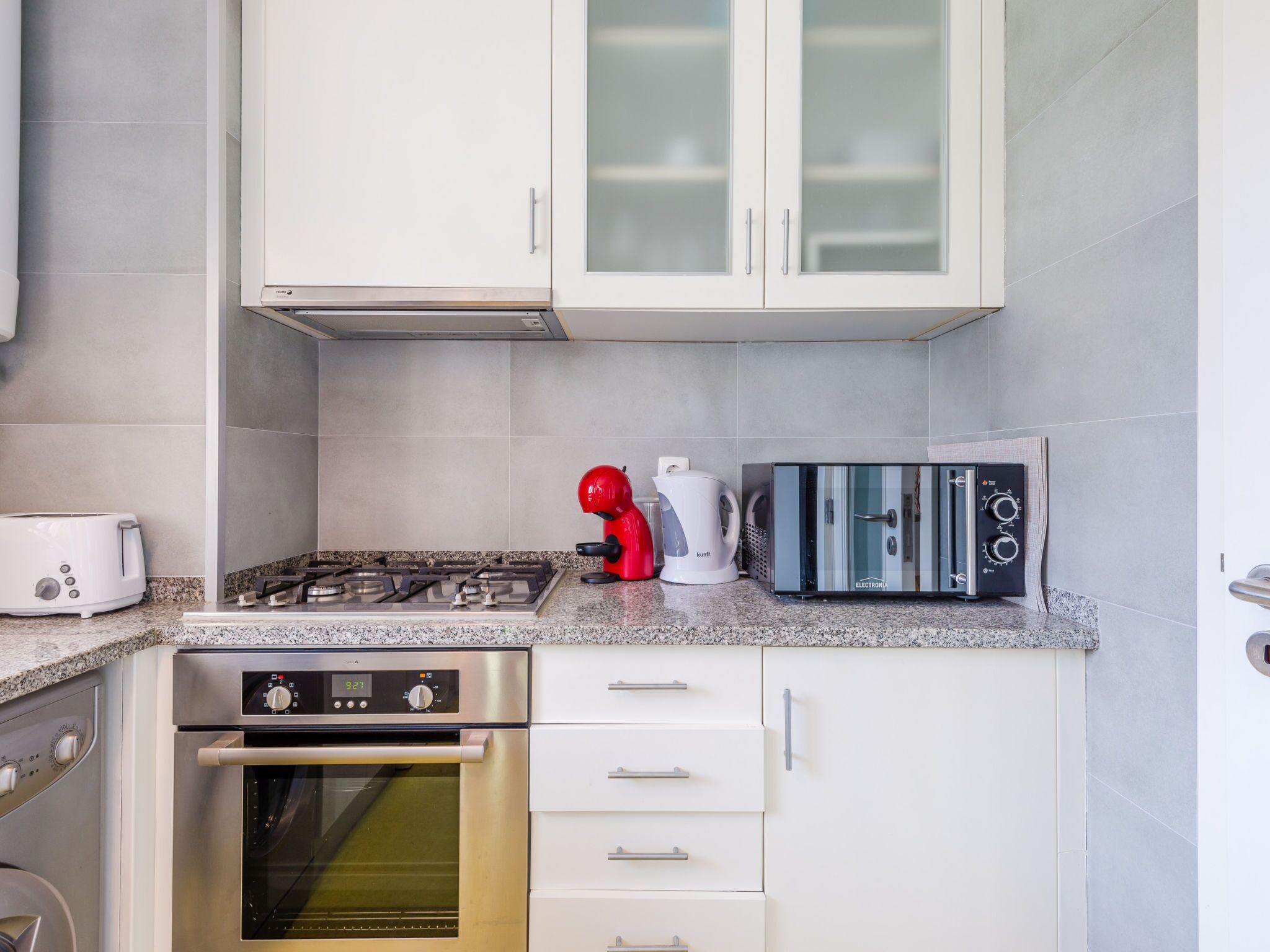 A modern kitchen with white cabinets, a gas stove, a toaster, a kettle, and an oven.
