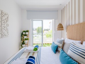 A modern bedroom with a large bed, striped pillows, a view of the outdoors, and a decorative wall piece. - Apartment  by Interhome (Albufeira)