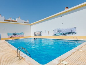 A swimming pool with clear blue water, surrounded by a tiled deck and a white wall with murals. - Apartment  by Interhome (Albufeira)