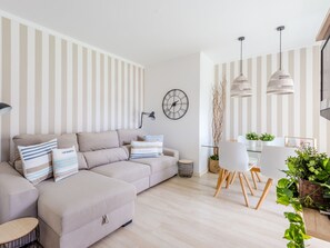 A modern living room with a sofa, a dining table with chairs, a clock, and striped wallpaper. - Apartment  by Interhome (Albufeira)