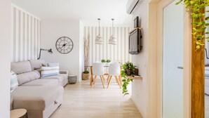 Ett modernt vardagsrum med en soffa, en matplats med stolar, en klocka, hängande lampor och en tv som är monterad på väggen.