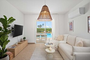 Ein modernes Wohnzimmer mit großem Fernseher, einem weißen Sofa, einem Essbereich mit Blick auf einen Pool und einer großen Korbtreleuchte.
