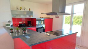 Une cuisine moderne avec un îlot central rouge, des appareils en acier inoxydable et un pare-feu en verre.