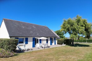 A house with a sloped roof, a patio with outdoor furniture, and a large tree in the background. - Holiday home in Santec on Dossen beach (Santec)