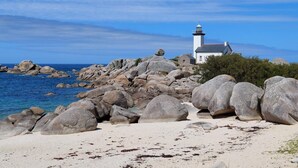 Un phare se dresse sur une côte rocheuse, au bord d’une eau d’un bleu limpide.