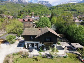 A traditional chalet with a stone facade, a wooden porch, and a view of a mountainous village. - Family home 5 minutes from the lake and in the heart of Talloires village (Talloires-Montmin)