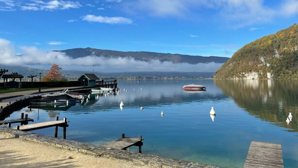 Ein ruhiger See mit einem Steg, einem Boot und einem Berg im Hintergrund.