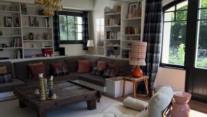 Ein Wohnzimmer mit einer Eckcouch, einem Couchtisch, einem Lesesessel und einem Bücherregal.