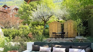 Ein überdachter Außenbereich mit Sitzgelegenheit, einer Couch und einem Holler Shed in einem üppigen Garten.