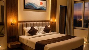 A modern hotel room with a large bed, a headboard with built-in lighting, a wall-mounted artwork, and a window with curtains. - VANU GROUP OF HOTEL - GRANDSON (Jaipur)