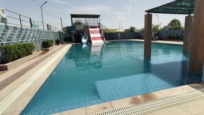 A swimming pool with a water slide, a covered area, and a brick wall. - VANU GROUP OF HOTEL - GRANDSON (Jaipur)