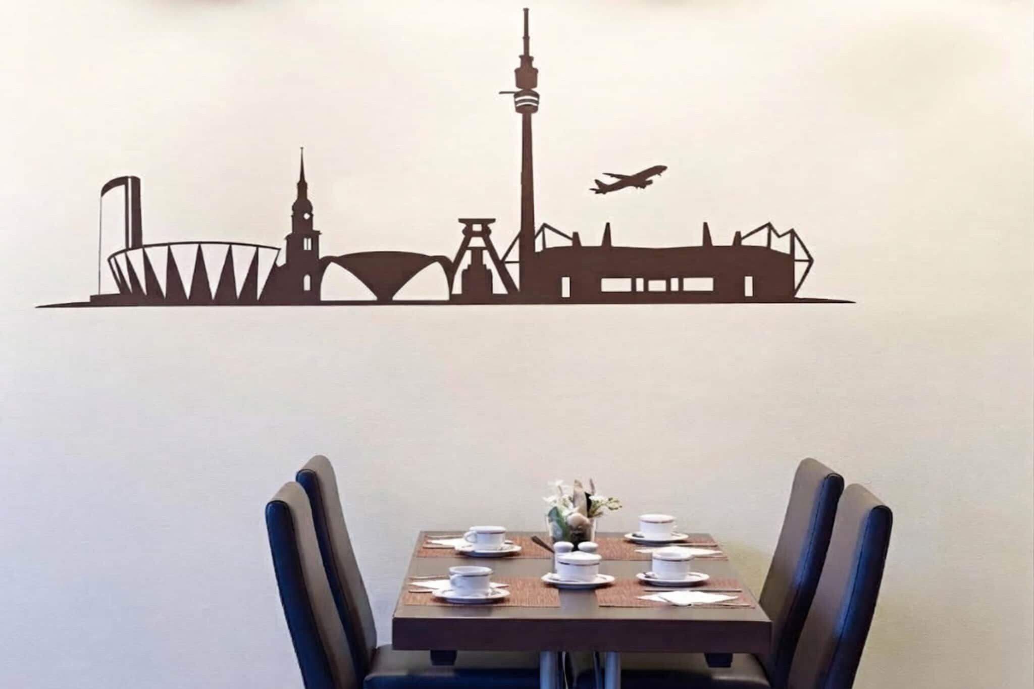 Ein Essbereich mit einem Tisch für zwei Personen, Stühlen und einer Wanddekoration, die eine Stadtansicht zeigt.