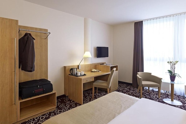 A hotel room with a bed, a desk with a chair, a wardrobe, a television, and a small table with a plant. - Sunday Hotel Dortmund Standard Single Room (Dortmund)