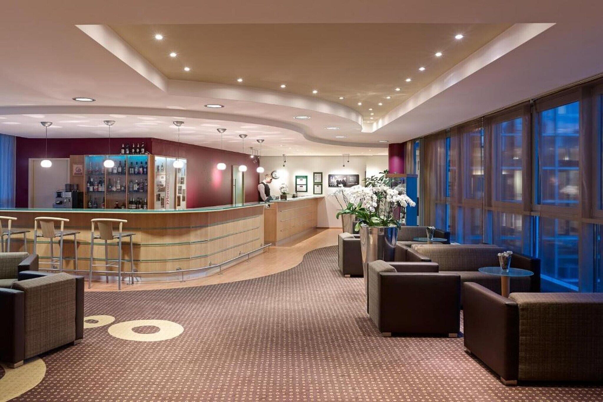 Eine Hotelhalle mit Rezeption, Sitzgelegenheiten und großen Fenstern.