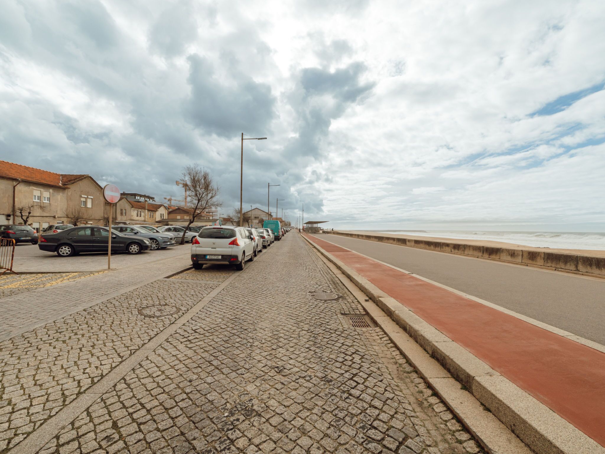 Uma rua de calçada com carros estacionados e um passeio vermelho que leva ao mar.