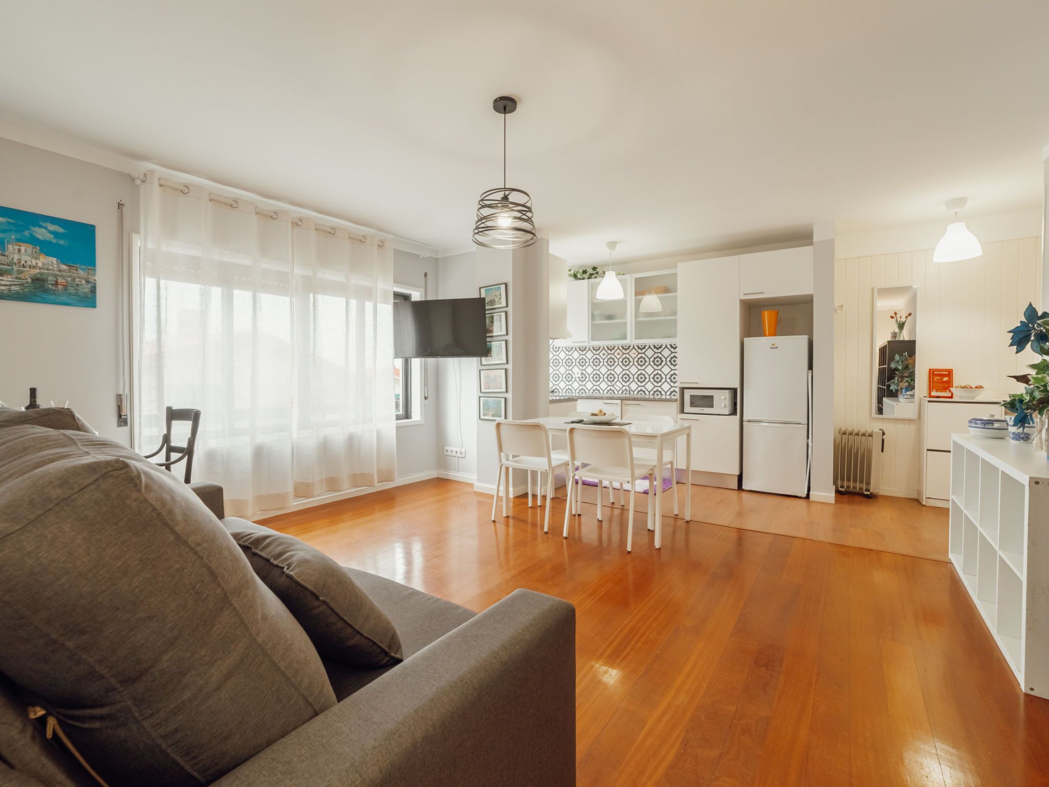 Una sala de estar moderna con un sofá, un comedor con sillas, una cocina equipada y un ventanal con cortinas.